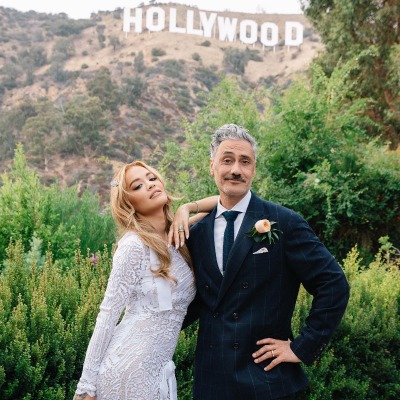 Matewa Kiritapu's father, Taika Waitit, and Rita Ora posing in front of the Hollywood hills in their wedding attire. 